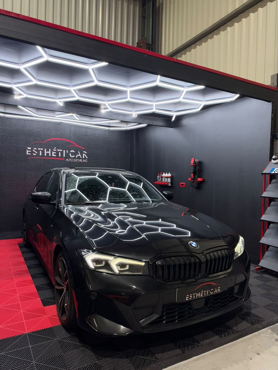 BMW Série 3 noire sous l'éclairage en nid d'abeille de l'atelier Esthéti'Car