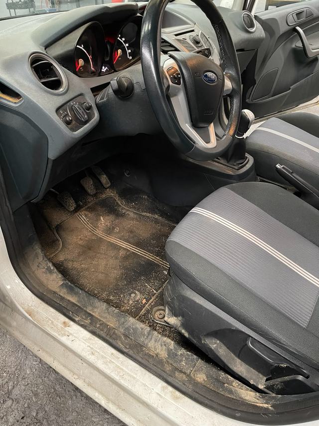Ford Fiesta avant nettoyage : tapis couvert de terre et seuil boueux